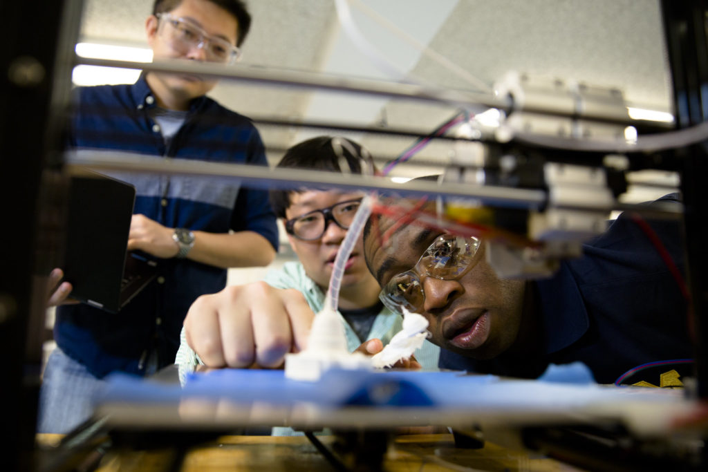 Molong Duon and Deokkyun Yoon, and Chinedum Okwudire, examine 3D printing equipment.