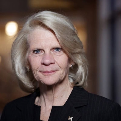 Karen Thole smiles at the camera/ She has blonde hair and blue eyes and is wearing a black suit with a U-M lapel.