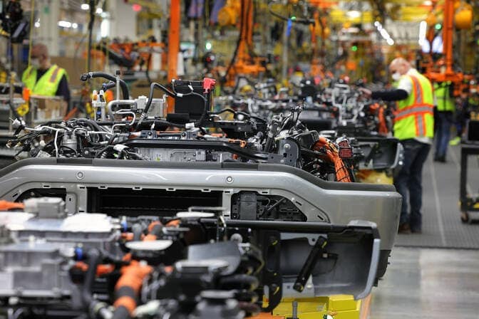 Workers wear safety gear and work at an automotive assembly line